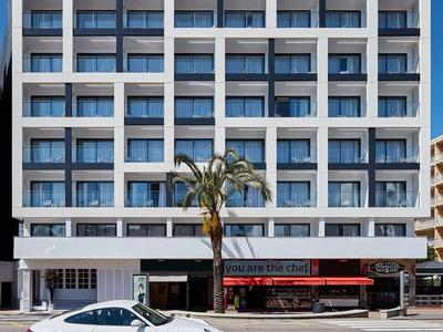 Edificio de hotel blanco moderno con balcones y un restaurante rojo en la planta baja.