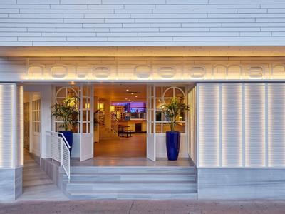 Entrada elegante de vestíbulo de hotel con fachada de vidrio, escaleras y plantas decorativas.