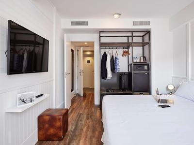 Modernes Hotelzimmer mit weißem Bett, hölzernem Boden und offenem Kleiderschrank mit Koffer.