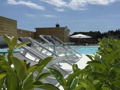 Piscina con tumbonas y plantas verdes bajo un cielo azul con nubes.