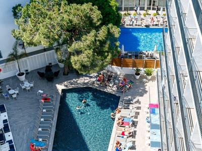 Vista aérea de un hotel con dos piscinas y tumbonas en la terraza.