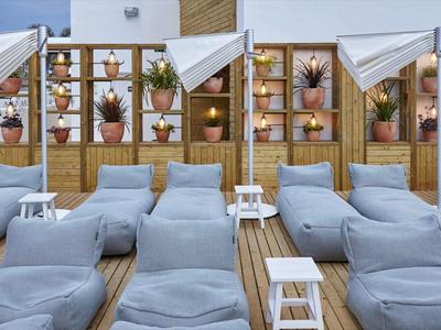 Terraza en la azotea con tumbonas grises y mesas, decorada con macetas y elementos de madera modernos.