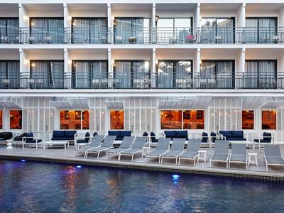 Piscina moderna de hotel con tumbonas y balcones en el fondo al anochecer.