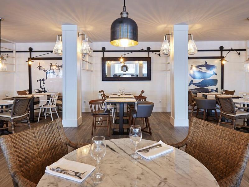 Área acogedora de restaurante de hotel con mesas redondas y sillas, paredes claras e iluminación moderna.