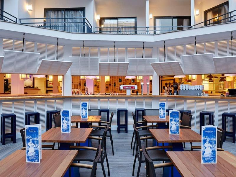 Área de restaurante moderna de un hotel con mesas y sillas bajo un techo redondo luminoso.