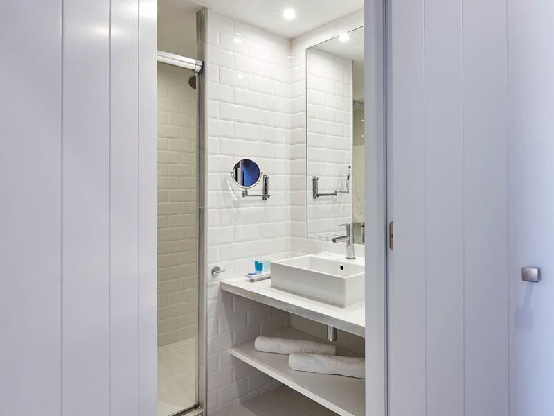 Baño con lavabo moderno, espejo y cabina de ducha en una habitación de hotel.
