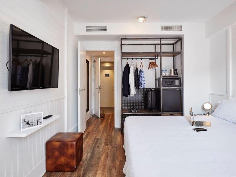 Habitación de hotel moderna con cama blanca, armario abierto y televisor montado en la pared.