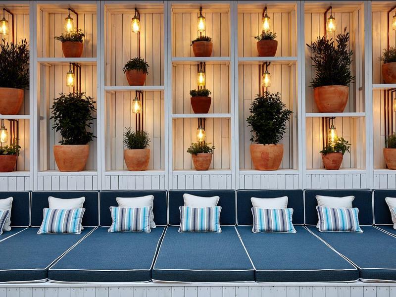 Cómodas tumbonas frente a una pared decorativa con plantas y luz cálida.