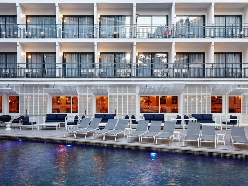 Piscina moderna de hotel con tumbonas y balcones en el fondo al anochecer.