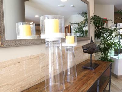 Three lit candles in glass holders on a wooden table in front of a large mirror.