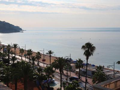 Coastal promenade with palm trees along a calm sea under a partly cloudy sky.