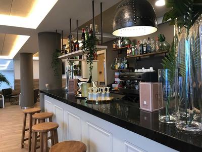 Modern hotel bar area with stools, black counter, and plants in a bright room.