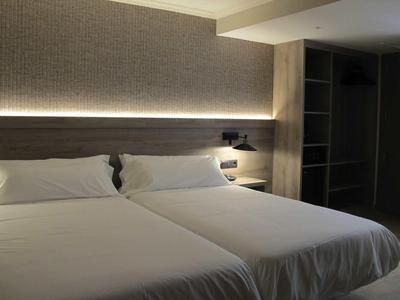 Modern hotel room with two single beds and indirect lighting.
