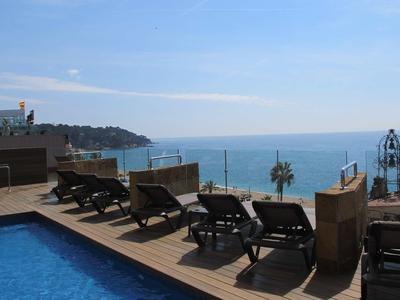 Pool area with lounge chairs overlooking the sea under a clear sky.
