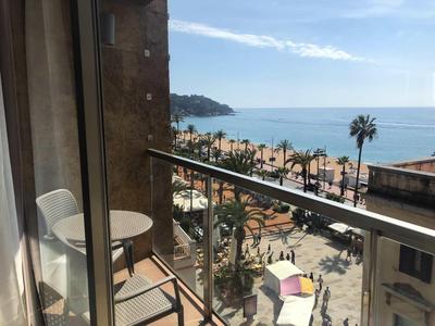 Balcon avec deux chaises et une table donnant sur une promenade de plage avec des palmiers et la mer.