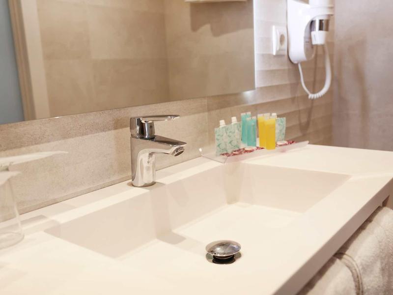 Modern hotel bathroom vanity with sink, mirror, hairdryer, and toiletries.