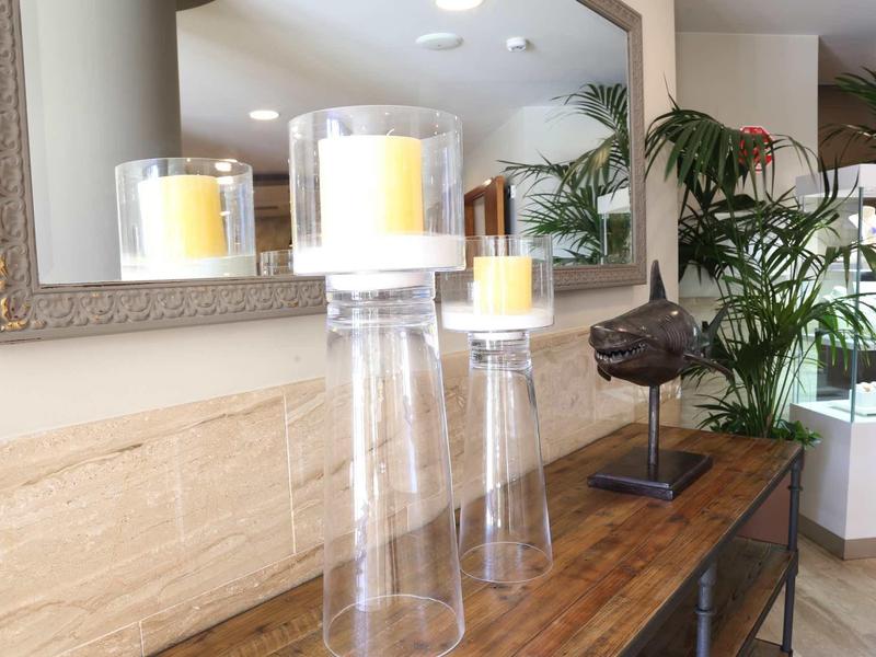 Three lit candles in glass holders on a wooden table in front of a large mirror.