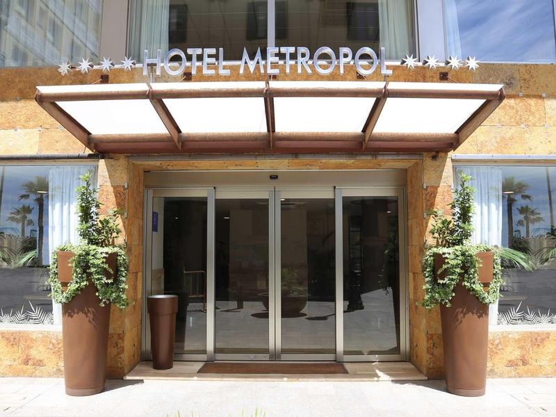 Entrance of Hotel Metropole with glass doors and large potted plants