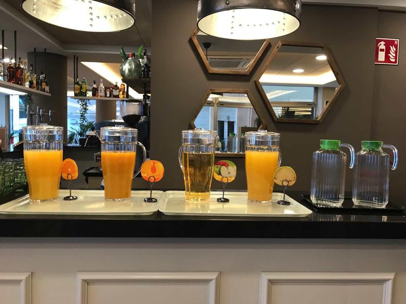 Counter with glasses filled with orange juice and water in front of a wall with hexagonal mirrors and lamps.