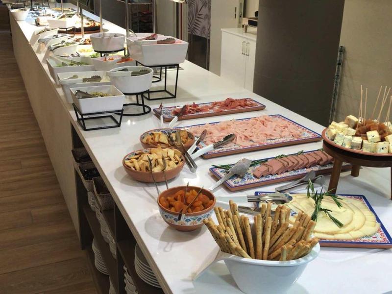 Long buffet with various foods like bread, cold cuts, and cheese in a modern room.