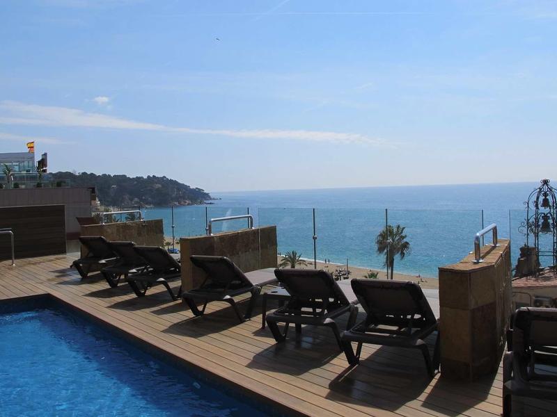 Pool area with lounge chairs overlooking the sea under a clear sky.