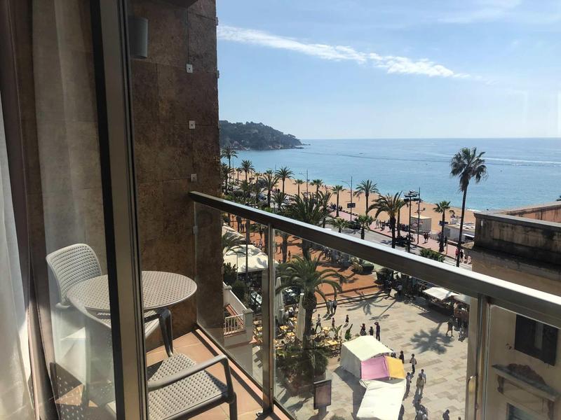 Balcony with table and chair overlooking beach and sea under clear sky.