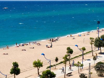 Sunny beach with blue umbrellas, walking path, and turquoise ocean waters.