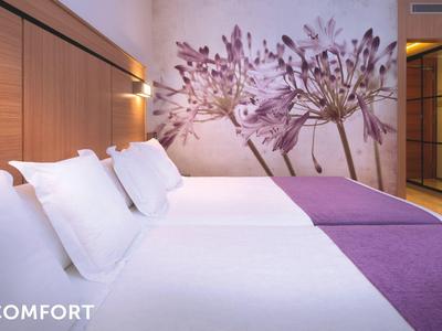 Modern hotel room with a large bed, white linens, purple accents, and floral wall art.