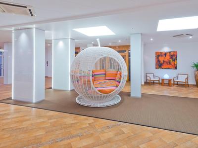 A spacious hotel lobby features modern hanging chair and bright seating area with artwork.