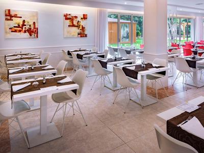 Bright and modern restaurant with white furniture, large windows, and abstract wall art.