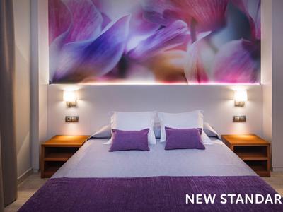 Bed with purple pillows and blanket, wooden nightstands, and a large floral artwork above.