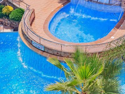 Curved pool with clear blue water and green plants around it.