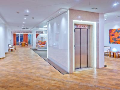 Hotel corridor with wooden floor, elevator, modern art, and seating area in warm lighting.