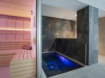 Modern sauna area with wooden benches and an adjacent hot tub with blue lighting.