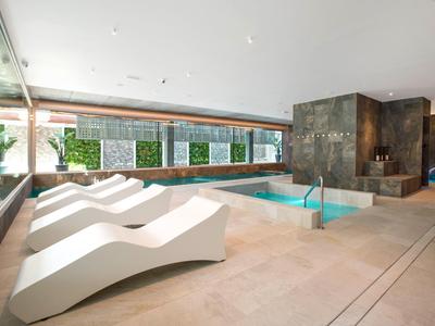 Modern indoor pool area with white lounge chairs and green wall panels behind.