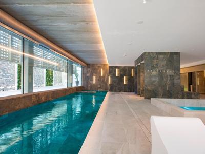 Indoor hotel pool with large windows and modern lighting along a wooden ceiling.