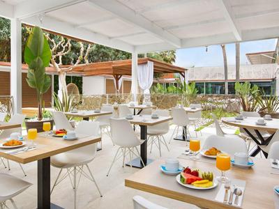 Outdoor hotel dining area with white tables and chairs, set with breakfast items and tropical plants.