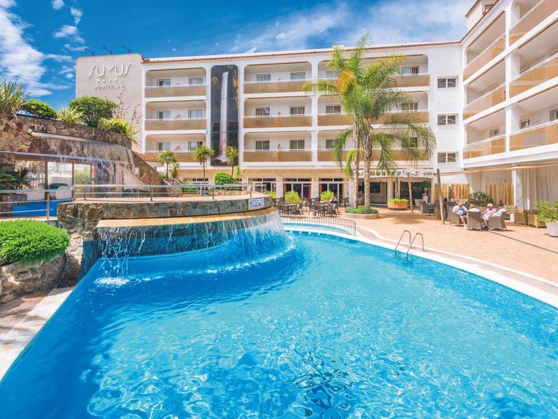 Hotel with outdoor pool, palm trees, and lounge chairs under a blue sky.
