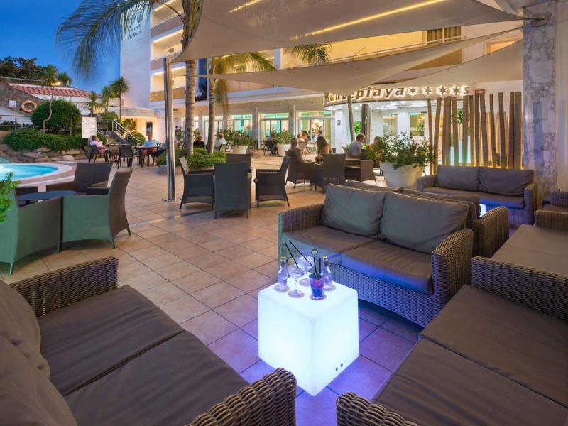 Outdoor hotel lounge area with wicker sofas, glowing tables, and poolside palm trees at dusk.
