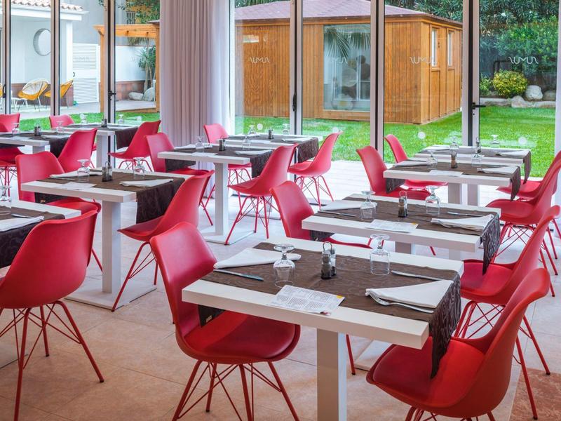Modern dining area with red chairs and tables set for meals near large windows.
