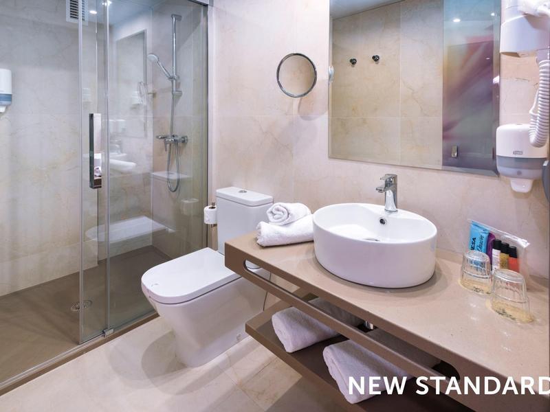Modern hotel bathroom with glass shower, round sink, and neatly arranged toiletries.