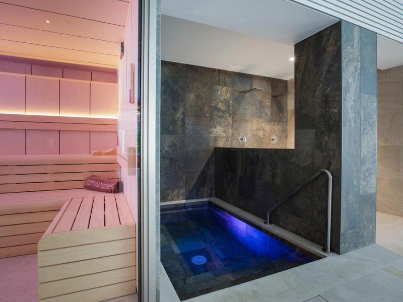 Modern sauna area with wooden benches and an adjacent hot tub with blue lighting.