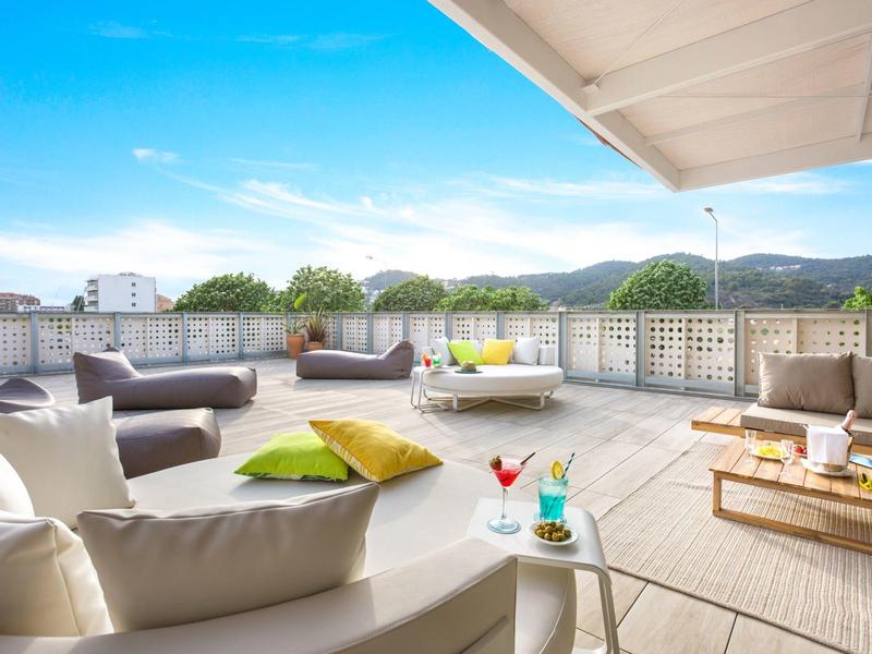 Spacious rooftop terrace with cozy sofas, colorful cushions, and a clear blue sky.
