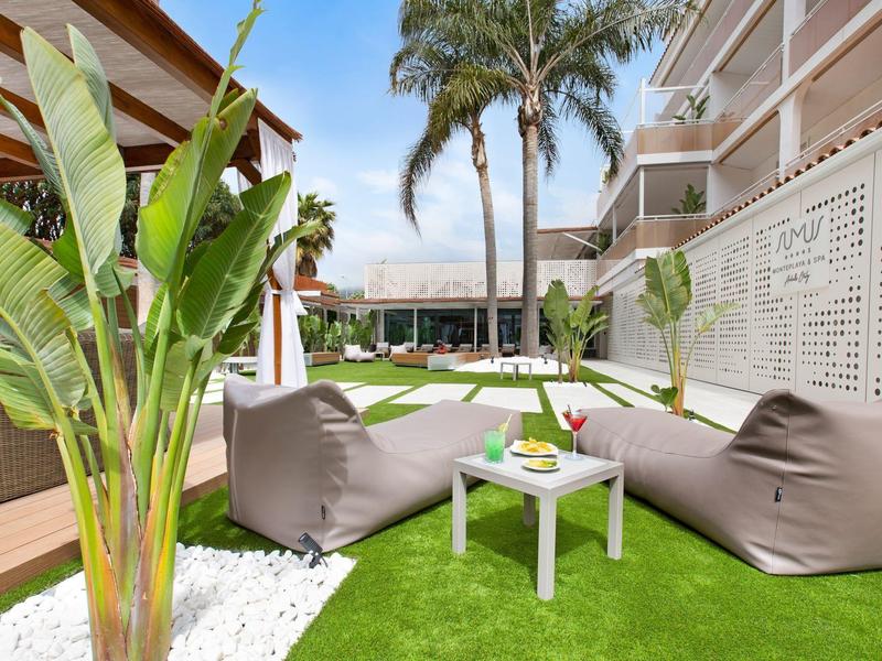 Outdoor seating area with bean bags, small table, tropical plants, and palm trees by a hotel.