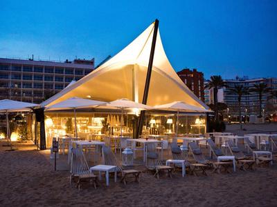 Restauracja na plaży z nowoczesnym namiotowym dachem i strefami wypoczynkowymi o zmierzchu.