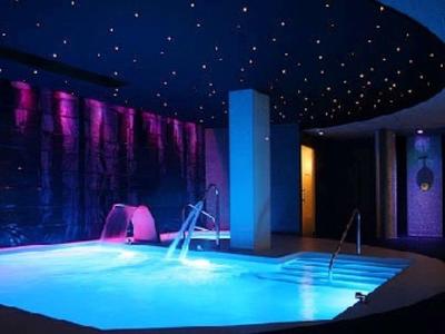 Nowoczesny kryty basen z wodospadem i sufitem z gwiazdami w relaksującej atmosferze.