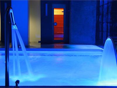 Oświetlony jacuzzi z dyszami wodnymi w niebieskim i pomarańczowym świetle w nowoczesnym wnętrzu.