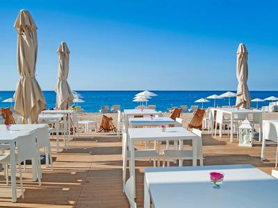 Pusta przestrzeń tarasu z białymi stołami i krzesłami blisko plaży pod niebieskim niebem.