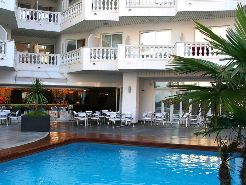 Dziedziniec hotelowy z niebieskim basenem, miejscami do siedzenia i białymi balkonami.