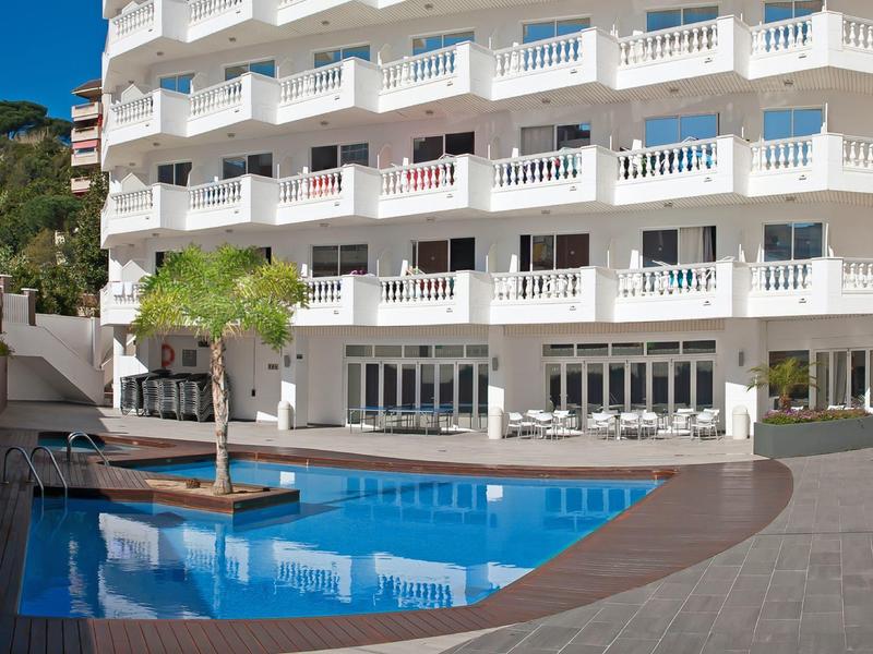 Nowoczesny kompleks hotelowy z wieloma balkonami i dużym basenem na zewnątrz przed budynkiem.